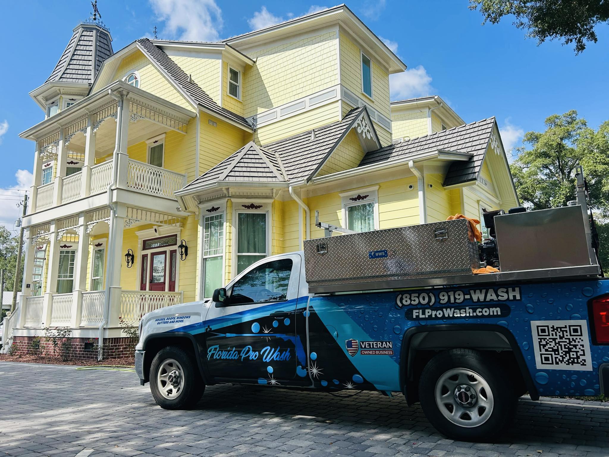 Florida Pro Wash truck parked in front of a large, yellow Victorian home in Panama City Beach. The truck, equipped for pressure washing, features the company's logo and contact information: (850) 919-WASH. Showcasing house washing services.
