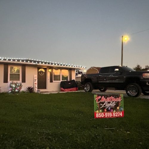 Home with Christmas light installation along the roofline. A truck is parked in the driveway, and a sign reads "Christmas Lights 850-919-9274".